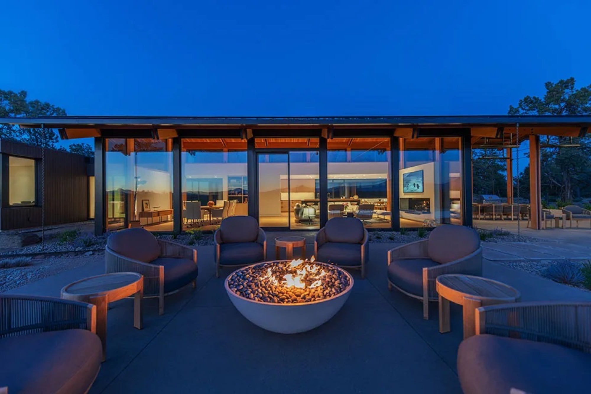 Custom mountain home at dusk with warm wood ceilings, black-framed glass, and a lit fire pit