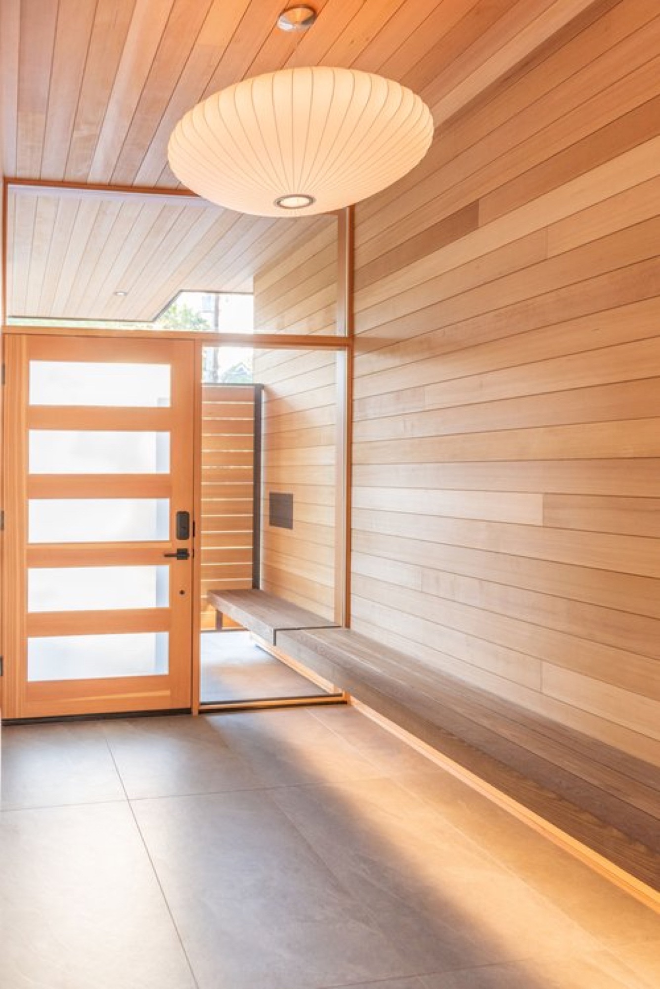Warm wood-paneled front entry with a modern pendant light