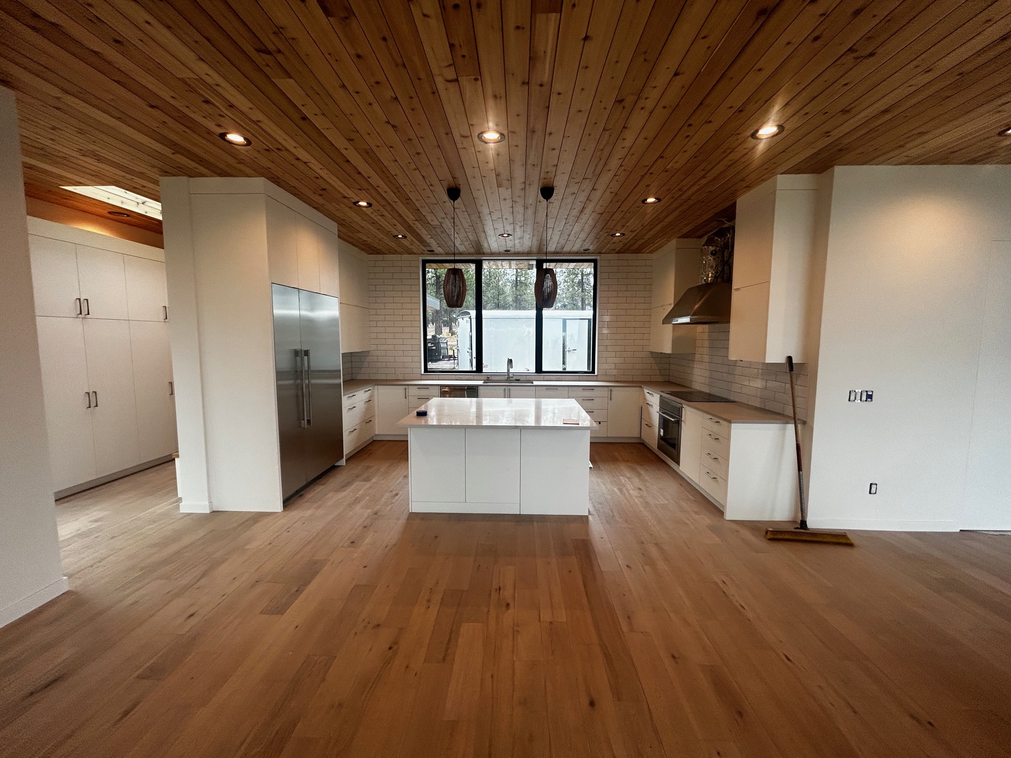 Open custom kitchen with wood ceiling, white island, and large windows